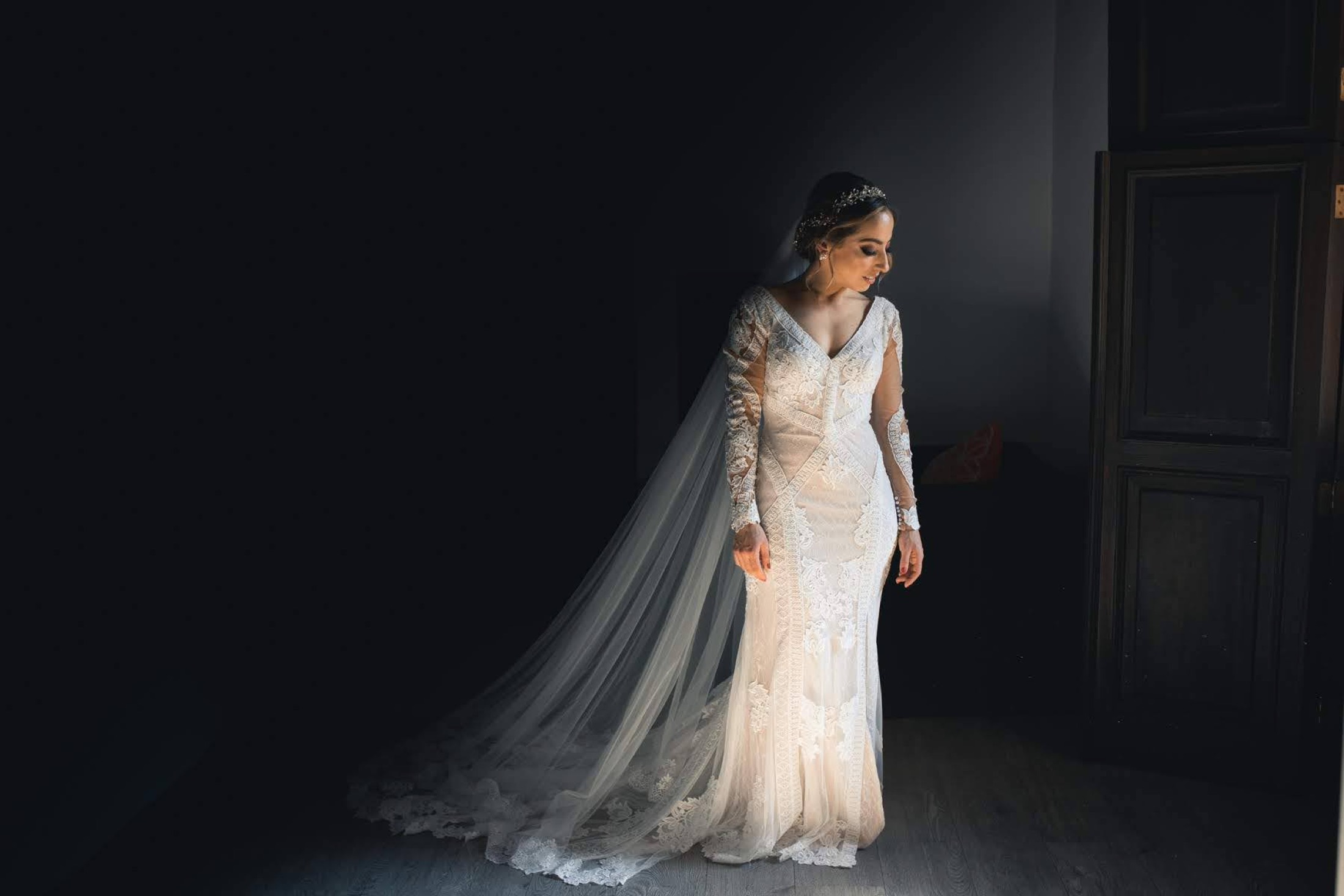 Novia con velo largo iluminada en un salón en penumbra, retrato editorial de bodas en Veracruz.