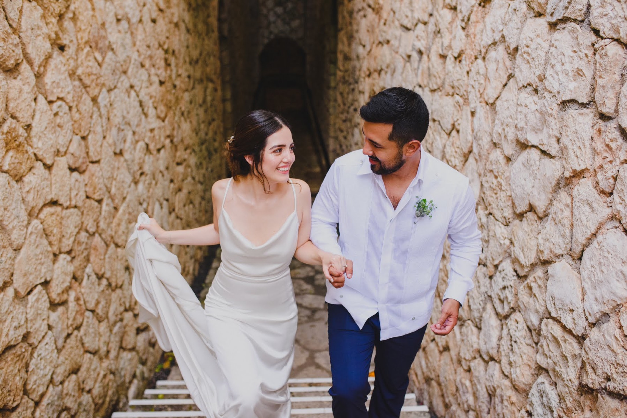 Novios subiendo una escalinata de piedra tomados de la mano, boda de destino en México.