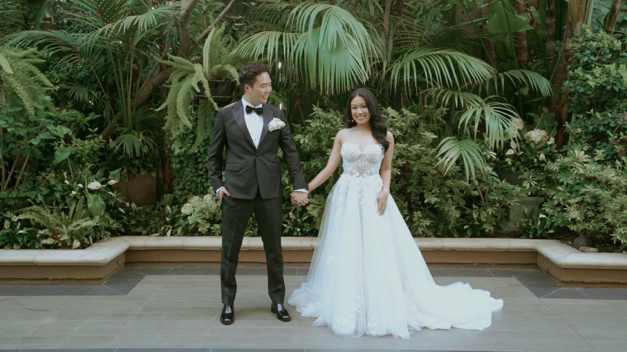 Novios tomados de la mano en un jardín tropical, boda de destino en México.