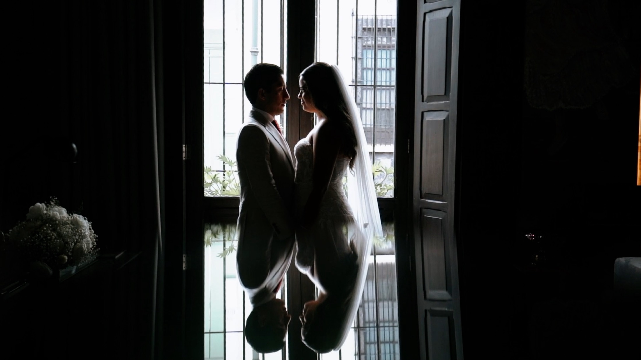 Novios en silueta frente al ventanal con su reflejo en el suelo, fotografía de bodas elegante.
