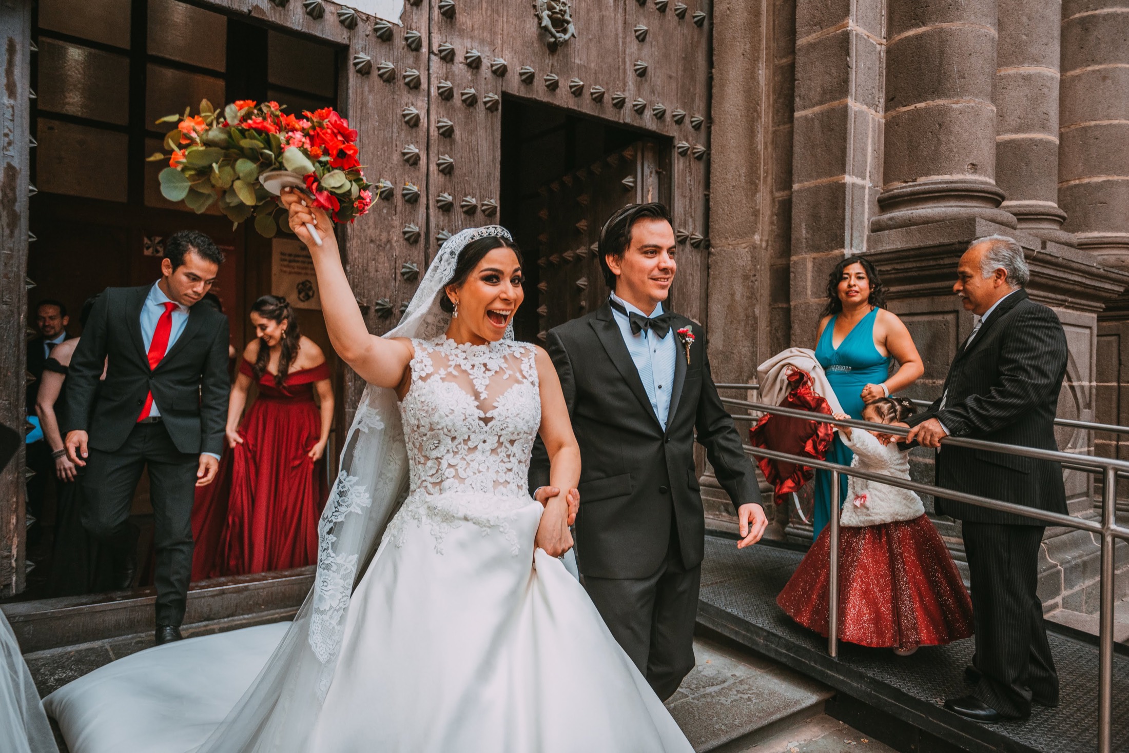 Salida de los novios de la catedral con el ramo en alto entre los invitados, fotografía de bodas en México.