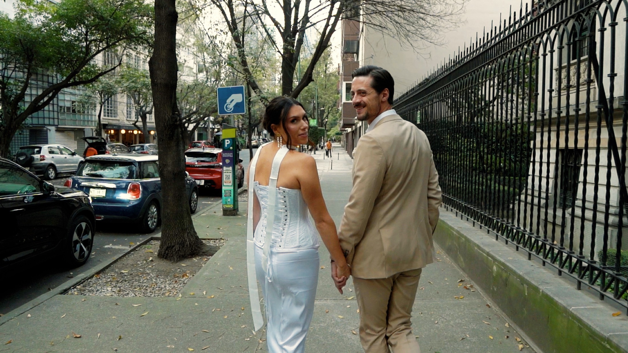 Novios caminando tomados de la mano por una calle arbolada en su sesión de pareja, por Miguel Beltrán, fotógrafo de bodas de destino.