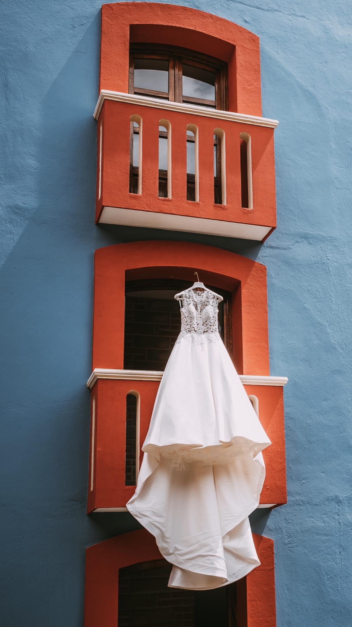Vestido de novia colgado en una fachada colonial azul y naranja, fotografía de bodas en México.